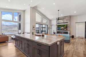Kitchen featuring open floor plan, a stone fireplace, light stone countertops, a ceiling fan, and light wood-style flooring