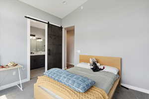 Carpeted bedroom with lofted ceiling, ensuite bath, and a barn door