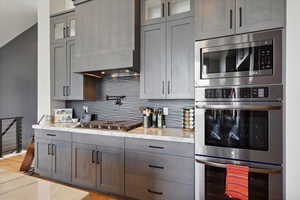Kitchen featuring stainless steel appliances, glass insert cabinets, decorative backsplash, and light stone countertops
