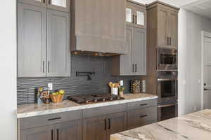 Kitchen featuring backsplash, glass insert cabinets, custom exhaust hood, and light stone countertops