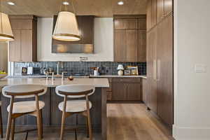 Kitchen featuring light wood-style flooring, a breakfast bar, decorative backsplash, pendant lighting, and paneled refrigerator