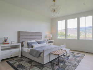 Expansive bedroom with light wood-finish flooring, three large gridded windows, a decorative chandelier, recessed lighting, and white baseboards