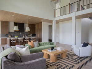 Open-concept living space featuring high ceilings, wood-finish flooring, a kitchen island with seating, a dark tile backsplash, and a second-story balcony with metal railings