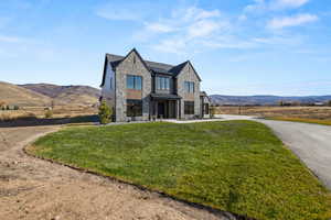 View of front of home with a mountain view, a standing seam roof, stone siding, a metal roof, and a front lawn