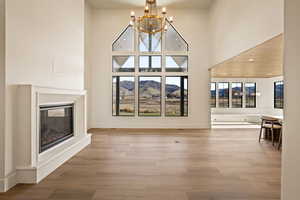 Unfurnished living room featuring a chandelier, a mountain view, a towering ceiling, light wood-style floors, and a glass covered fireplace