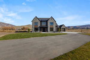 View of front of home with a mountain view, stone siding, a front lawn, and driveway