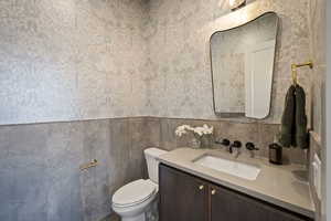 Bathroom featuring vanity, wallpapered walls, and wainscoting