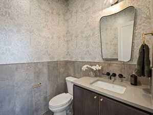 Bathroom featuring vanity, wallpapered walls, and wainscoting