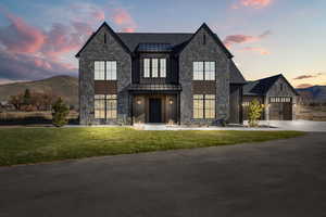 Modern inspired farmhouse featuring stone siding, a standing seam roof, a front yard, and driveway