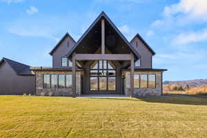 Back of property with stone siding, a patio, a lawn, and board and batten siding