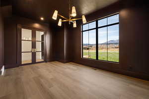 Spare room with a mountain view, french doors, light wood-type flooring, a chandelier, and a textured ceiling