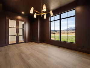 Spare room with a mountain view, french doors, light wood-type flooring, a chandelier, and a textured ceiling