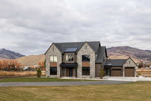 View of front of house with stone siding, a mountain view, a standing seam roof, driveway, and a front lawn