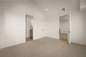 Unfurnished bedroom featuring vaulted ceiling, recessed lighting, ensuite bathroom, and light carpet