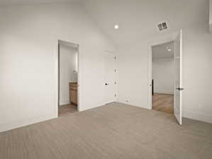 Unfurnished bedroom featuring vaulted ceiling, recessed lighting, ensuite bathroom, and light carpet