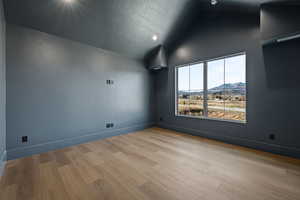 Spare room featuring a mountain view, a textured ceiling, vaulted ceiling, and light wood-style floors