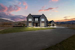 View of front of property featuring stone siding, a mountain view, curved driveway, a lawn, and a garage