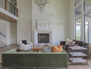 Open-concept living area with a double-height ceiling, large windows, a grand fireplace, and wood-finish flooring