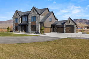 View of front of home featuring stone siding, a mountain view, a front yard, and driveway