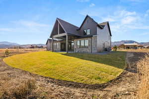 Back of property with a mountain view, a patio, stone siding, and a lawn
