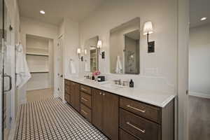 Full bathroom with a spacious closet, double vanity, recessed lighting, and a stall shower
