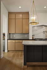 Kitchen featuring pendant lighting, dark cabinets, light wood finished floors, tasteful backsplash, and dark stone counters