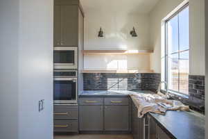 Kitchen featuring gray cabinets, open shelves, dark countertops, stainless steel appliances, and decorative backsplash