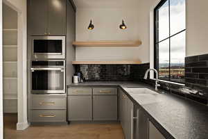 Kitchen featuring gray cabinetry, stainless steel appliances, open shelves, light wood finished floors, and decorative backsplash