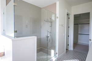 Full bath featuring a shower stall, a walk in closet, and tile patterned floors