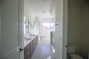 Full bath featuring double vanity, a shower stall, a freestanding tub, and dark tile patterned flooring