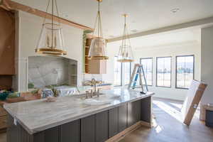 Kitchen with a kitchen island with sink, wood finished floors, hanging light fixtures, light stone counters, and recessed lighting