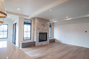 Unfurnished living room featuring beamed ceiling, light wood finished floors, a stone fireplace, plenty of natural light, and recessed lighting