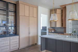 Kitchen with decorative backsplash, dark stone countertops, wood finished floors, and light brown cabinetry