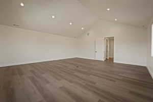 Empty room with dark wood finished floors, recessed lighting, and high vaulted ceiling