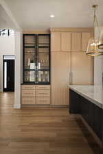 Kitchen with hanging light fixtures, light brown cabinetry, dark wood-style flooring, light stone counters, and dark cabinets