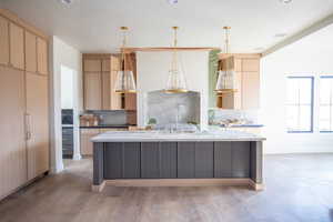 Kitchen with light brown cabinets, decorative backsplash, light stone counters, pendant lighting, and recessed lighting