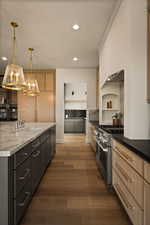 Kitchen with pendant lighting, dark wood-style floors, dark stone counters, range with two ovens, and recessed lighting