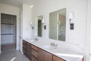 Bathroom featuring double vanity, dark tile patterned flooring, a walk in closet, and a shower