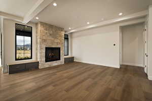 Unfurnished living room featuring dark wood-style floors, beam ceiling, a stone fireplace, and recessed lighting