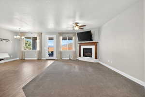 Unfurnished living room with plenty of natural light, a brick fireplace, a chandelier, a textured ceiling, and a ceiling fan