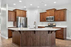 Kitchen with a breakfast bar, appliances with stainless steel finishes, recessed lighting, an island with sink, and light wood-style floors