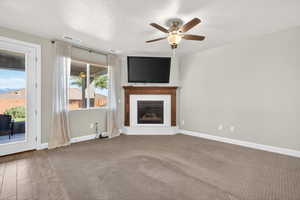 Unfurnished living room featuring a fireplace, a textured ceiling, a ceiling fan, and carpet