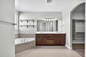 Bathroom featuring a bath, double vanity, a walk in closet, and light tile patterned floors