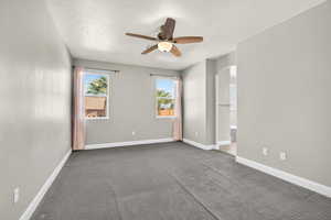Carpeted empty room featuring arched walkways, a textured ceiling, and ceiling fan