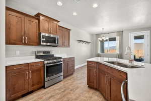 Kitchen featuring appliances with stainless steel finishes, decorative light fixtures, brown cabinets, recessed lighting, and a textured ceiling