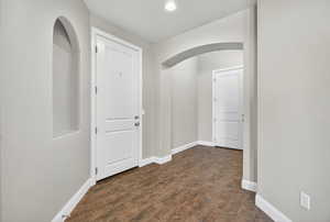 Hallway featuring arched walkways, dark wood-style flooring, and recessed lighting