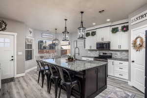 Kitchen featuring a kitchen bar, white cabinetry, backsplash, appliances with stainless steel finishes, and dark stone countertops