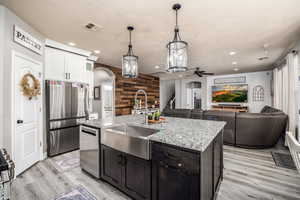 Kitchen featuring wooden walls, a ceiling fan, stainless steel appliances, hanging light fixtures, and light stone countertops
