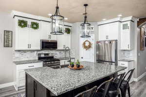 Kitchen with decorative backsplash, light wood-style flooring, appliances with stainless steel finishes, a kitchen island with sink, and recessed lighting