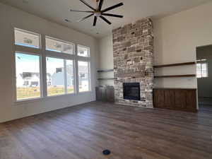 Unfurnished living room with dark wood finished floors, a fireplace, ceiling fan, and a high ceiling